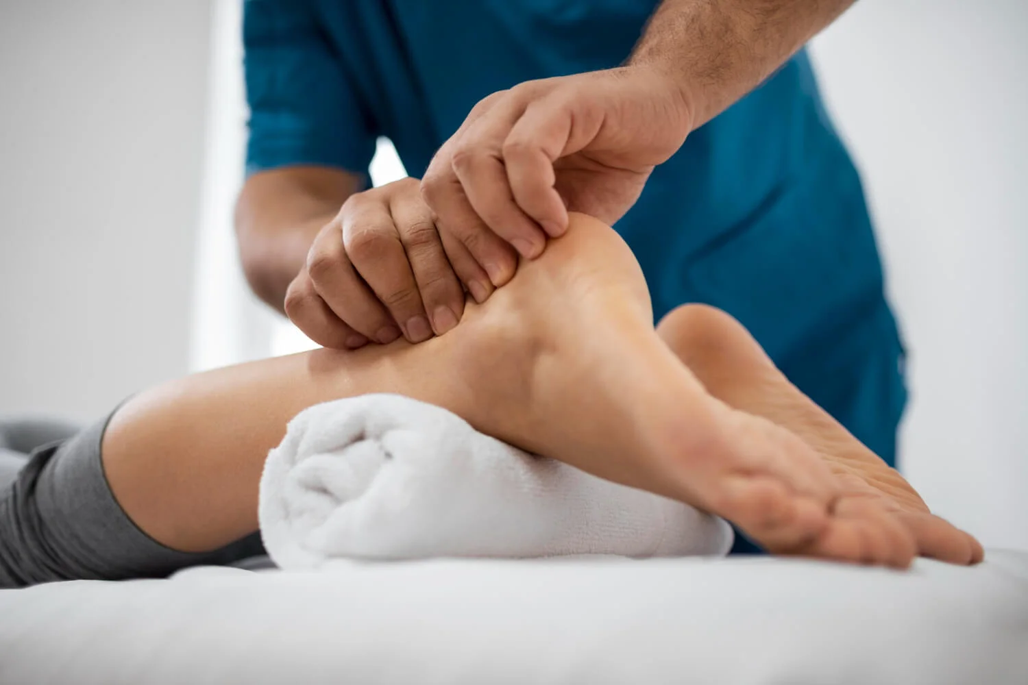 Therapist performing manual ankle therapy on a patient lying down, focusing on joint rehabilitation and pain relief